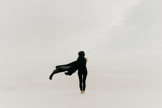 Dark mysterious black cloth blowing in the wind in the desolate desert covering a woman's silhouette