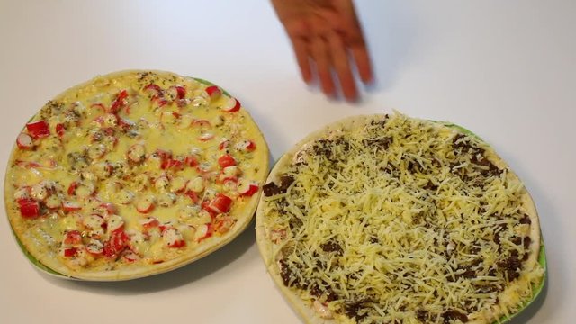 Preparation of pizza. The man puts on the table a ready pizza with crab sticks and picks up a pizza parcel with mushrooms.