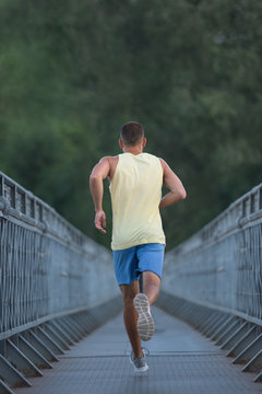 Anonymous sporty man jogging on pedestrian bridge outdoor