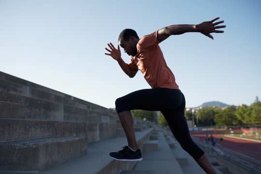 African black sportsman running upwards with energy on the stadium bleachers