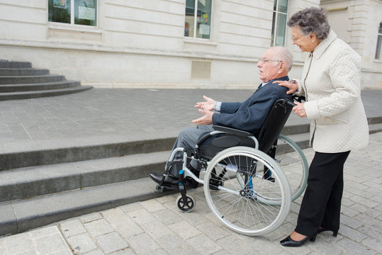 old man on wheelchair and woman carrying him