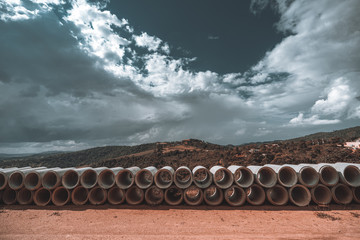 A wide-angle shooting of the rows of cement soil-pipes on the ground, used for the creation of the sewerage systems and the aqueducts, an overcast sky and the hills in the background