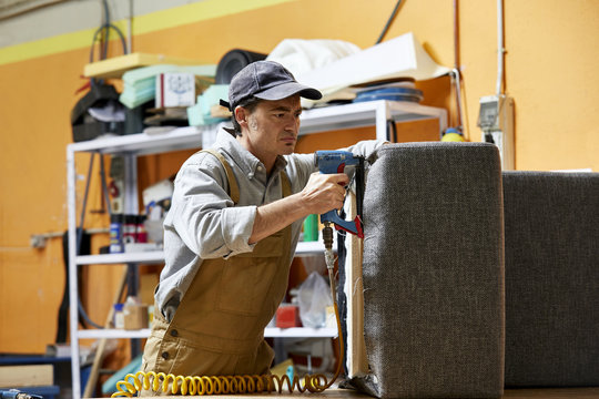 Worker Using Upholstery Gun While Making Sofa