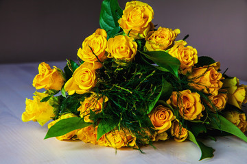 Bouquet of yellow roses is laying on the light wooden table without water