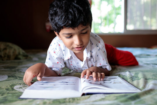 Young boy reads a book lying on bed