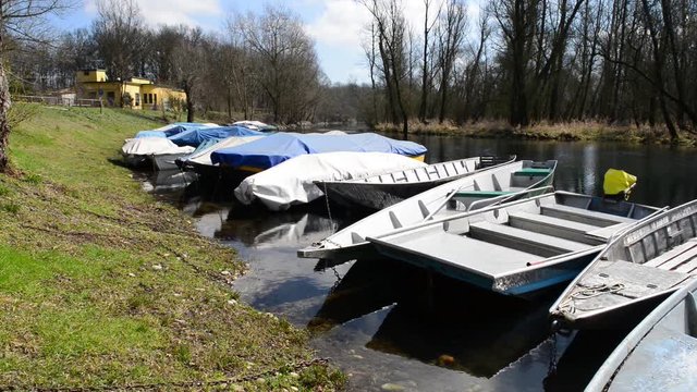 barche da fiume attraccate al molo coperte da teloni al primo sole dopo l'inverno