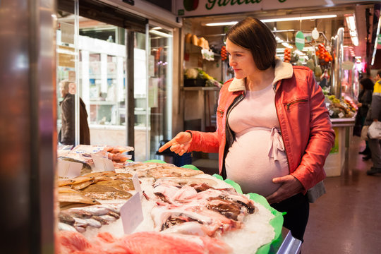 PREGNANT WOMAN BUYING FISH IN A MARKET HALL