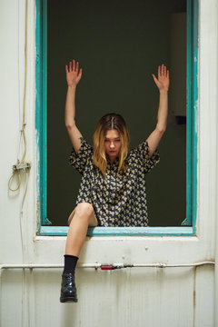 Girl in unglazed window with arms up and leg over frame.