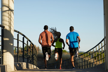 Two men and a young woman running together in the city at sunset