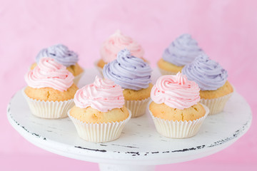 Cupcakes decorated with pink and violet cream on white shabby shic stand on pastel pink background.