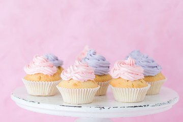 Cupcakes decorated with violet and pink buttercream on shabby shic stand on pastel pink background