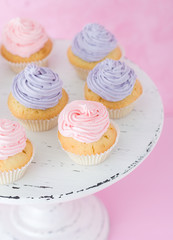 Cupcakes with violet and pink cream on white shabby shic stand on pastel pink background