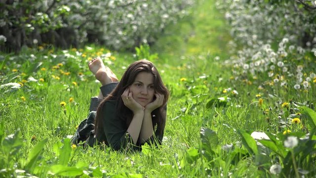 Young woman lying down on fresh grass in blossom orchard looking up to sky