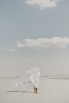 Human standing in desert with a white flow sheet blowing in the wind to the side