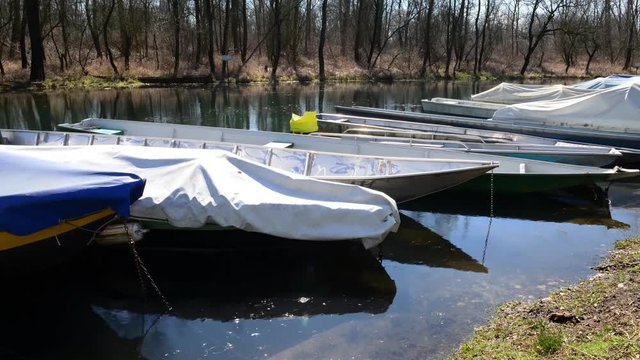 barche da fiume attraccate al molo coperte da teloni al primo sole dopo l'inverno