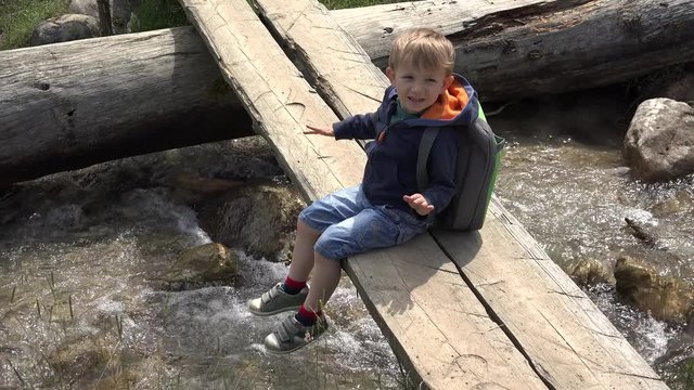 Little boy with a backpack resting on wooden bridge 