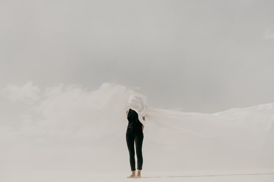 Contrast of woman wearing black with white fabric hiding her face in the minimal landscape
