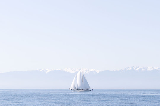 Single sailboat with full sail on water with mountain background