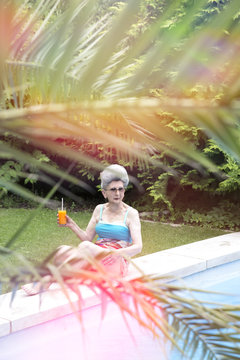 Senior woman relaxing with drink on poolside