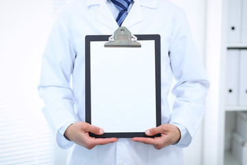 Unknown male doctor standing straight while holding medical clipboard with blank white paper. Medicine and health care concept