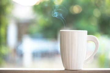 A white cup of coffee in the morning with smoke and colorful bokeh.