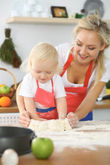 Little girl and her blonde mom in red aprons  playing and laughing while kneading the dough in the kitchen. Homemade pastry for bread, pizza or bake cookies