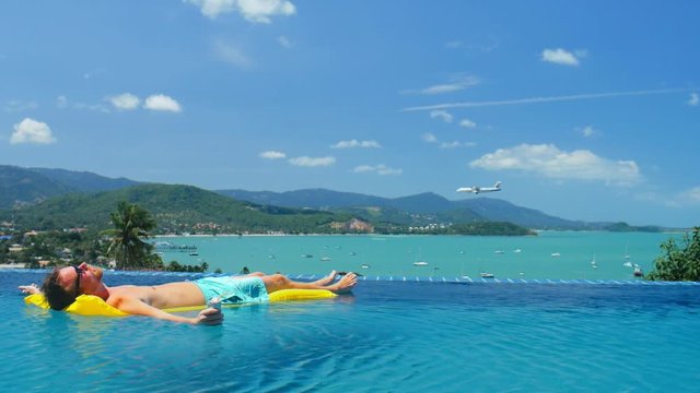 Rich man relaxing on yellow mattress in transparent water infinity pool