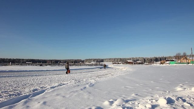 Two people walk on a snowy road in the village