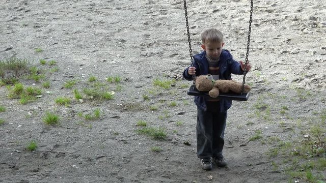 Little child pushing teddy bear  in the swing, innocent friendship