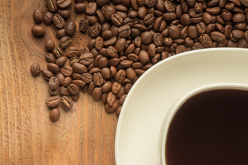 a cup of coffee is on a wooden table. scattered grains of coffee