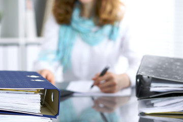 Binders with papers are waiting to be processed with businesswoman or secretary back in blur....