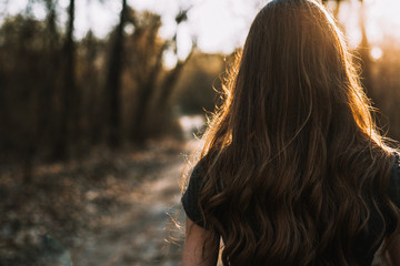 Rear view of sad young woman walking through park at sunset