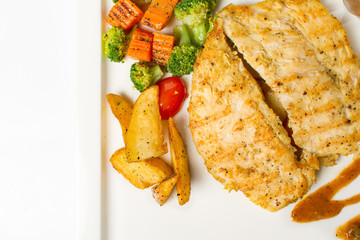 Grilled chicken breast with vegetable, baked potatoes, and a glass of black pepper gravy on white background
