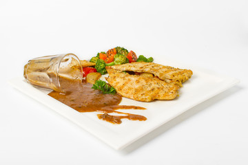 Grilled chicken breast with vegetable, baked potatoes, and a glass of black pepper gravy on white background