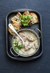 Mustard cream sauce stewed pork and grilled bread - delicious lunch on dark background, top view. Flat lay