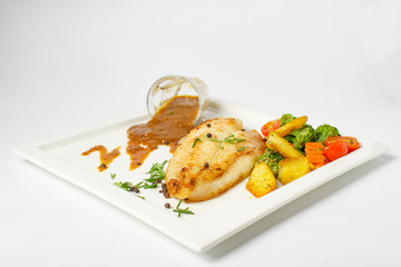 Grilled fish fillets steak served with mix vegetable, potatoes and a glass of black pepper gravy sauce on white background