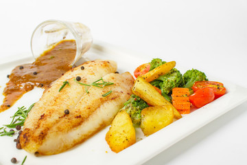 Grilled fish fillets steak served with mix vegetable, potatoes and a glass of black pepper gravy sauce on white background