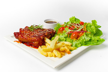 Roasted barbecue pork ribs served with french fries and salad on white background