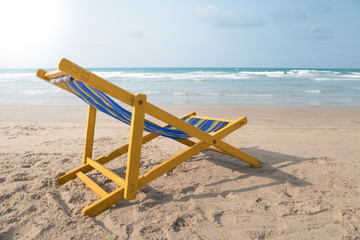 An yellow beach chair rests on the white sand of the beach and Bright blue sea with white clouds, at Rayong Thailand.