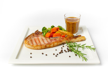 Grilled pork chop steak served with vegetable,fried potatoes and black pepper gravy on white background