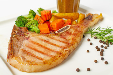 Grilled pork chop steak served with vegetable,fried potatoes and black pepper gravy on white background