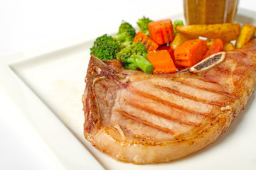 Grilled pork chop steak served with vegetable,fried potatoes and black pepper gravy on white background