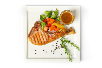 Grilled pork chop steak served with vegetable,fried potatoes and black pepper gravy on white background