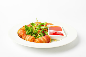 Fried sausages wrapped in bacon serve with mix vegetable, chili sauce and ketchup on white background