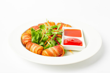 Fried sausages wrapped in bacon serve with mix vegetable, chili sauce and ketchup on white background