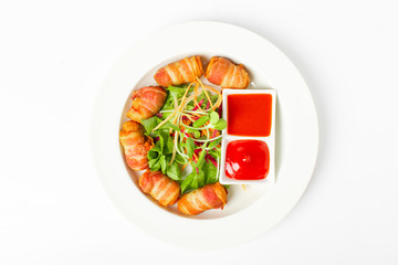 Fried sausages wrapped in bacon serve with mix vegetable, chili sauce and ketchup on white background