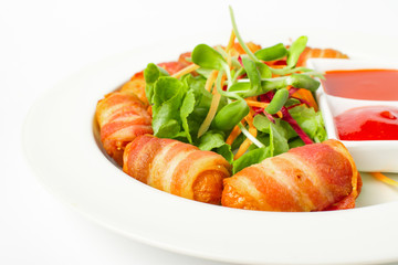 Fried sausages wrapped in bacon serve with mix vegetable, chili sauce and ketchup on white background