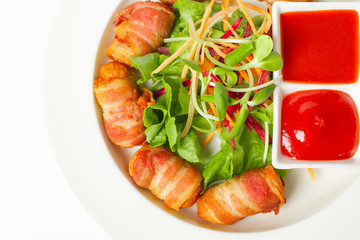 Fried sausages wrapped in bacon serve with mix vegetable, chili sauce and ketchup on white background