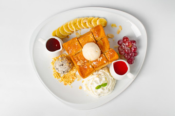 Desserts, Toast topped with vanilla ice cream, served with whipping cream, grape, banana, bean, honey and strawberry sauce on white background
