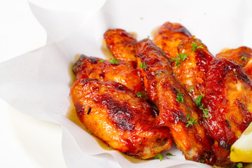 Grilled chicken wings with BBQ sauce. Garnish with lemon and coriander in a paper top view closeup on white background